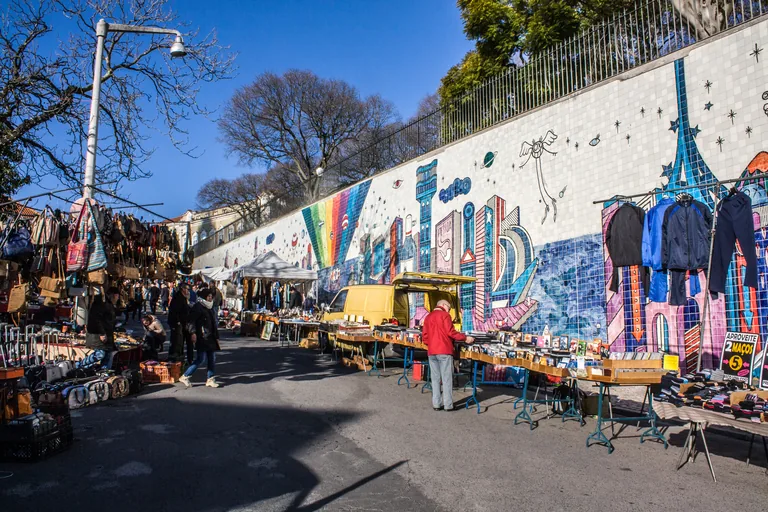 Stalls of clothes and bric a brac at the Feira da Ladra, along a wall of painted tiles.