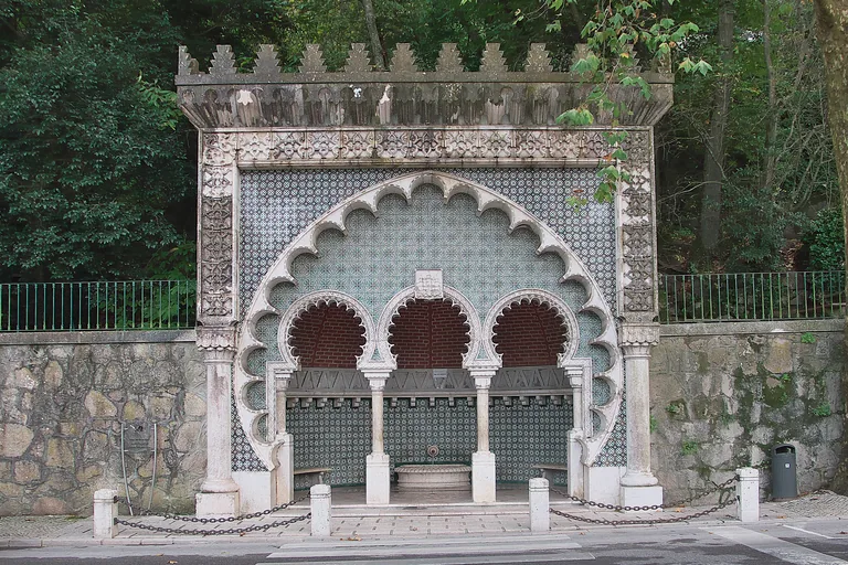 The Fonte Mourisca, a white stone fountain with a scalloped horseshoe arch around three smaller arches, framed in patterned tiles under stepped battlements.