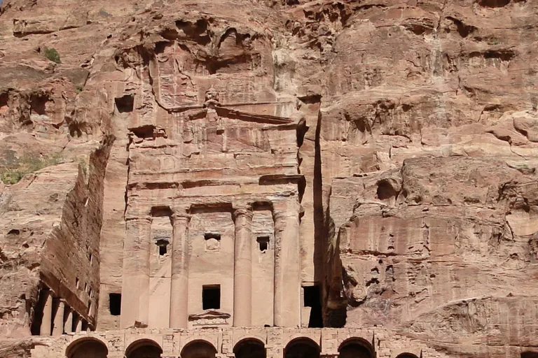 The front of the Urn Tomb, tall engaged columns and small niches cut into the cliff of Jabal Khubtha, above the row of arches that holds up its terrace.
