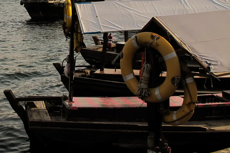 Abras moored at a landing on Dubai Creek, dark wooden hulls under pale canopies, with yellow life rings on a post in front and open water behind.
