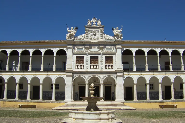 The arcaded courtyard of the University of Évora, with a marble fountain before the central pavilion crowned by statues.