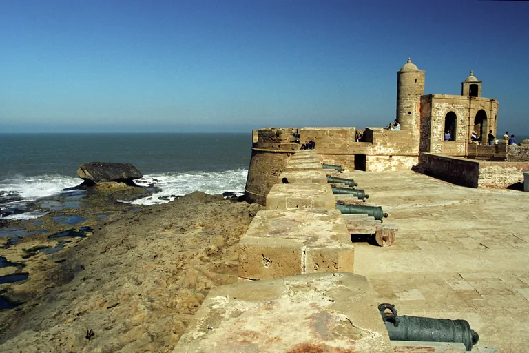 The stone sea rampart of the Skala de la Ville with a row of bronze cannons, a corner turret and a bastion above the rocks and the Atlantic surf.