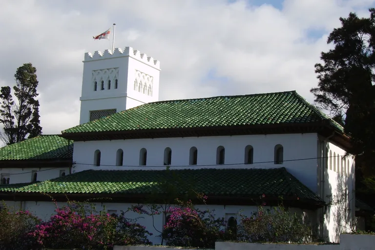 St Andrew's Church in Tangier, a white building with green tiled roofs and a square crenellated tower flying a flag, behind a garden wall and flowering bougainvillea.