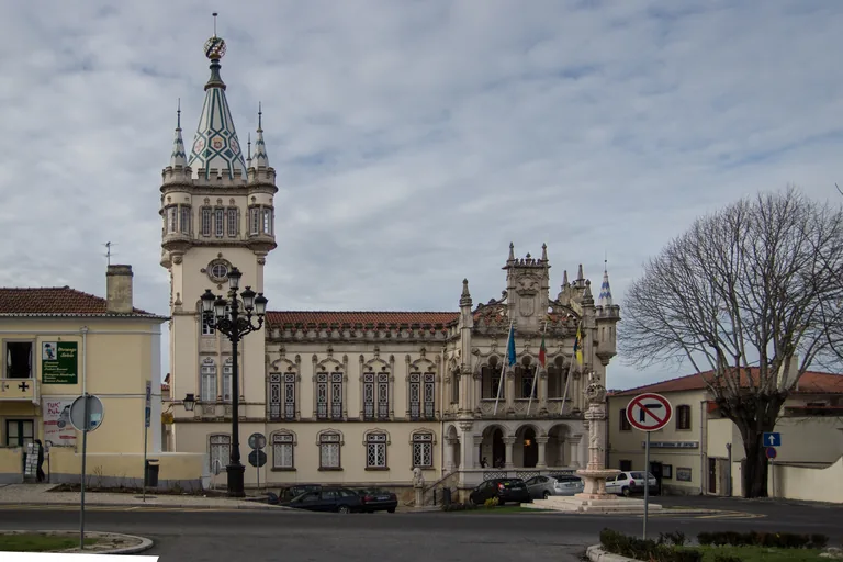 Sintra Town Hall seen across its square, with the tall tower under a steep tiled spire, the carved stone front and the marble fountain.