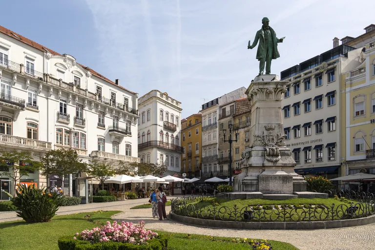 The statue of Joaquim António de Aguiar on its tall pedestal in Largo da Portagem, among flower beds and pale town houses.