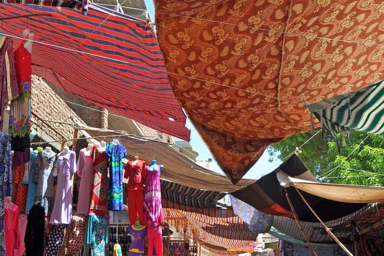Awnings of striped and patterned cloth stretched over the souq lane in Luxor, with dresses on mannequins and racks of clothes and sandals hanging below.