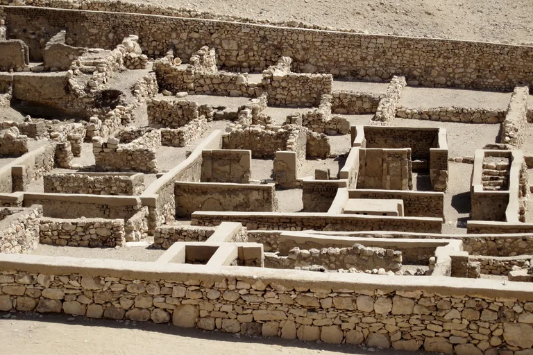 The stone footings and low walls of the village houses at Deir el Medina seen from above over the village wall, a grid of small rooms with doorways and a few plastered walls.