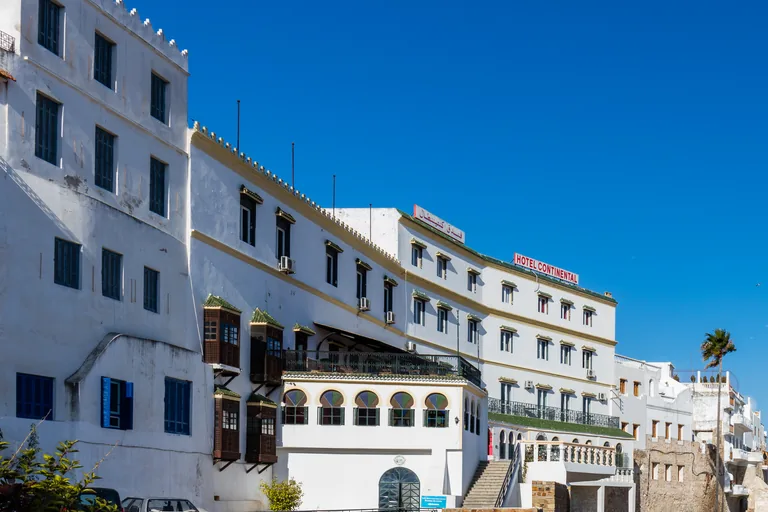 The long white front of the Hotel Continental at the edge of the old town, with its name in red letters, wooden balconies and green tiled roofs under a deep blue sky.