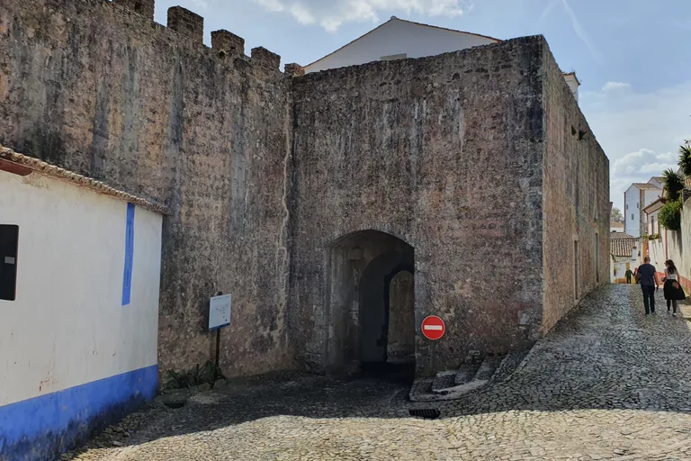 The Porta da Senhora da Graça, a dark arched passage through a massive stone tower in the town wall, with a cobbled lane climbing to the right.