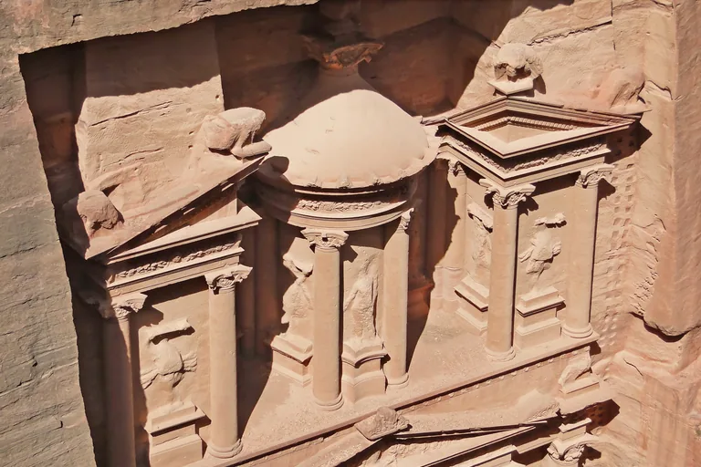 The upper storey of the Treasury's facade seen from above, a round central pavilion under a dome with carved figures between its columns, flanked by half pediments and a solid stone urn.