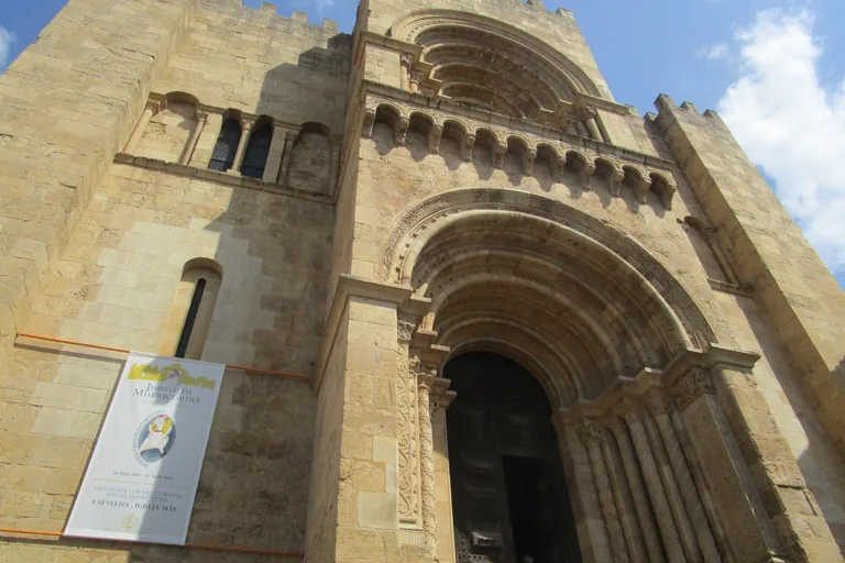 The crenellated Romanesque west front of the Old Cathedral, with its deep carved portal and a hanging banner.