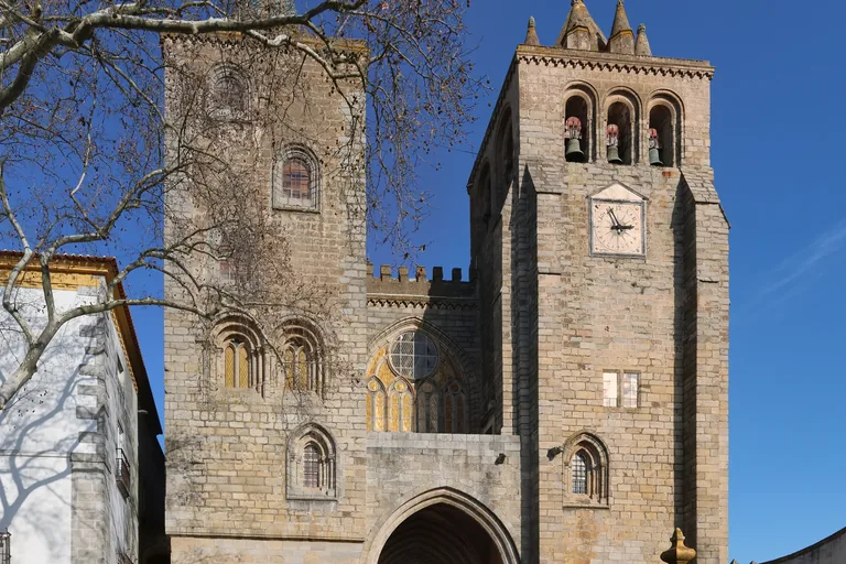 The west front of Évora Cathedral, with two unequal granite towers, the crenellated gallery between them and the top of the pointed portal.