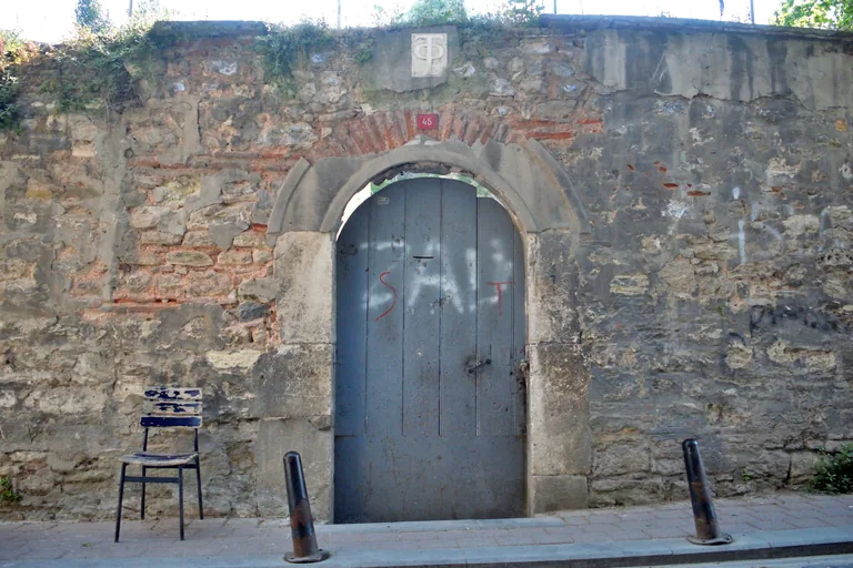 A grey metal gate in the high stone wall of the Metochion of the Holy Sepulchre.
