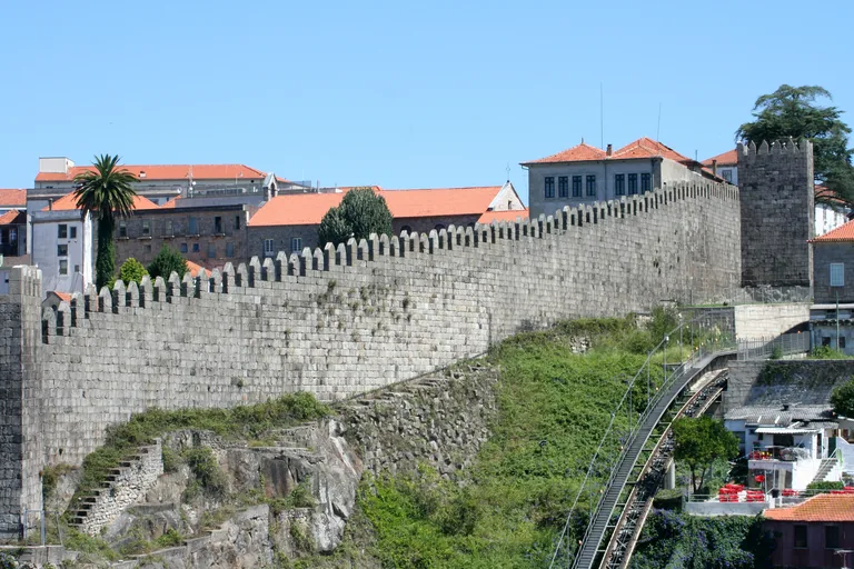 A crenellated stretch of the Fernandine Walls above a green slope, with the Guindais funicular track below.