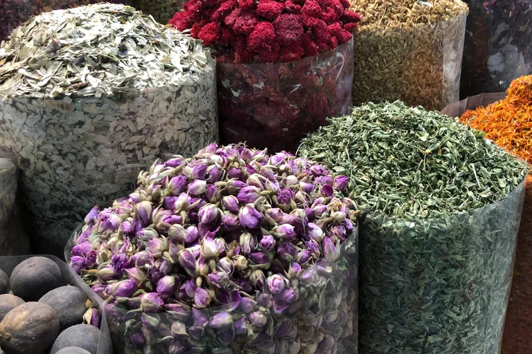Open sacks of dried rose buds, herbs, leaves, red flowers and safflower at a shop of the Deira spice souq, with dried limes at the lower left.