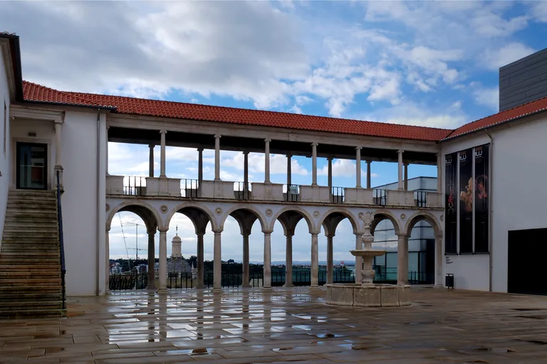 The arcaded loggia of the Machado de Castro museum courtyard, with a stone fountain and wet paving in front.