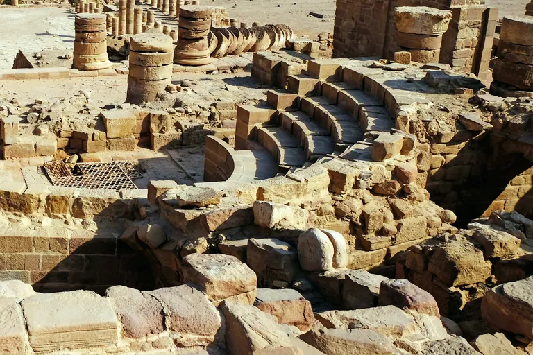 The small theatre inside the Great Temple seen from above, curved stone rows of seats around a paved floor, with column drums and fallen columns of the courts beyond.