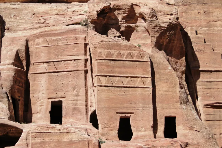 Two rock cut tomb fronts on the Street of Facades, each crowned with rows of stepped crow step decoration over a plain doorway, in rose coloured sandstone.