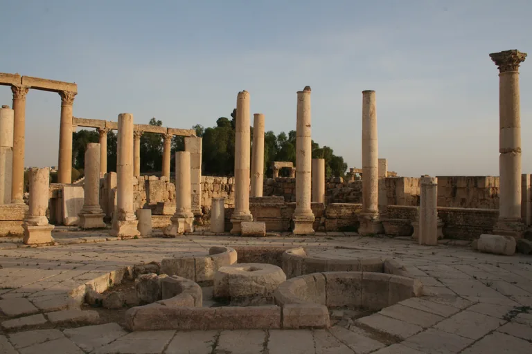 The market hall at Jerash, standing columns of the colonnaded street and the hall around a paved court, with the low curved stone walls of its central fountain in the foreground.