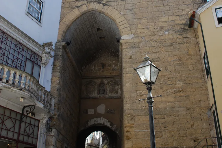 The deep arch of the Almedina Gate under its stone tower, with a carved panel inside the vault and a street lamp in front.