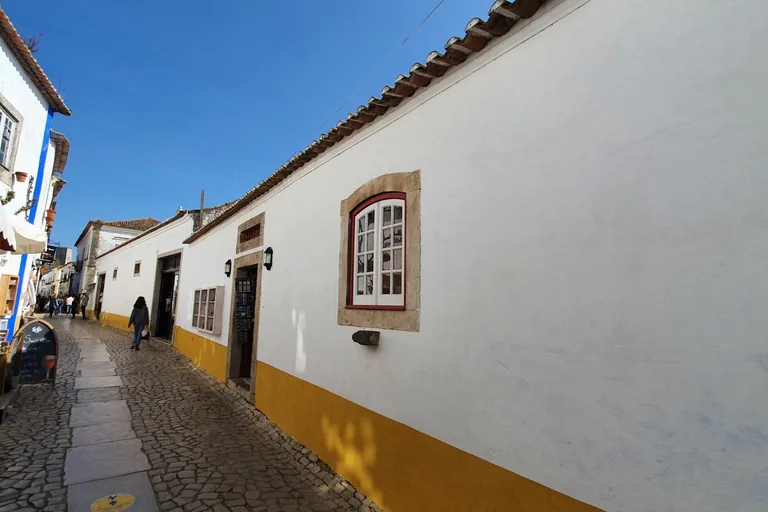 The narrow cobbled Rua Direita running uphill between whitewashed houses trimmed in yellow and blue, with a few people walking in the distance.