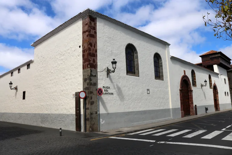 The corner of the Santa Catalina convent, long whitewashed walls with a pier of dark red stone, tall arched windows and arched wooden doors, and a carved wooden lookout on the roof at the far end.