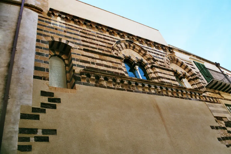 Striped stone arches on the upper facade of Cefalu's Osterio Magno.