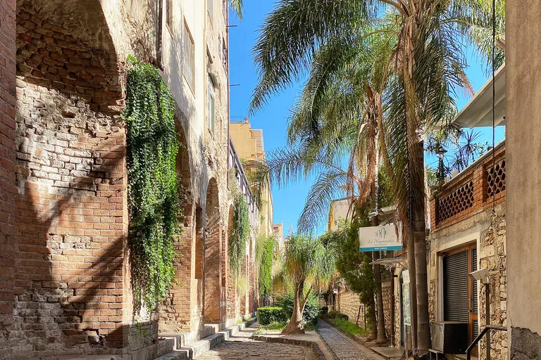 The long brick wall of Le Naumachie beside a narrow Taormina lane.