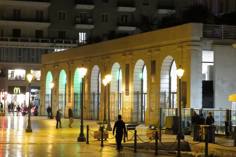 The illuminated arched facade of Spazio Murat on Piazza del Ferrarese at night.