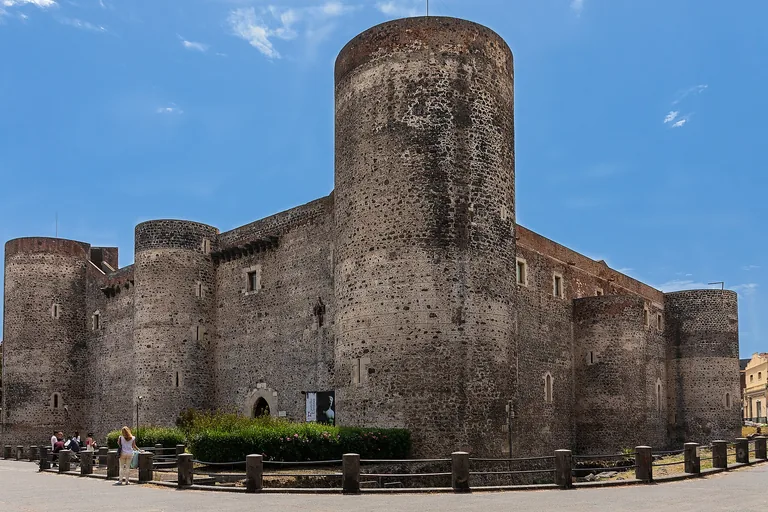 The round corner towers and dark-stone exterior of Ursino Castle in Catania.