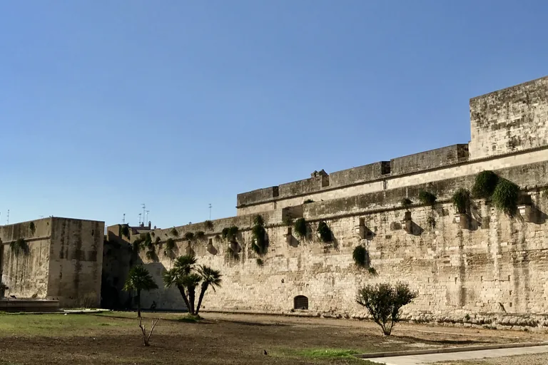 Long pale-stone bastion wall of Castello Carlo V beneath a clear sky.