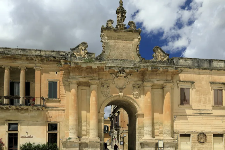 Porta San Biagio's sculpted arch and statue beneath a clouded sky.
